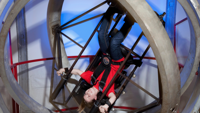 A smiling guest is flipped upside down inside the rings of the Multi-Axis Trainer