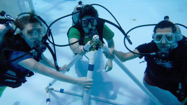 Three swimmers in SCUBA gear complete an underwater assembly