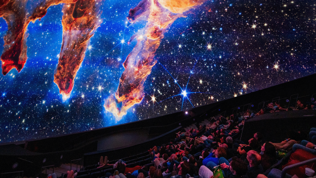 A seated audience looks up at a dome screen displaying images from the James Webb Telescope