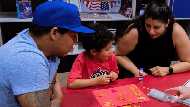 A family participates in a creative STEM activity with their young child in Spark!Lab